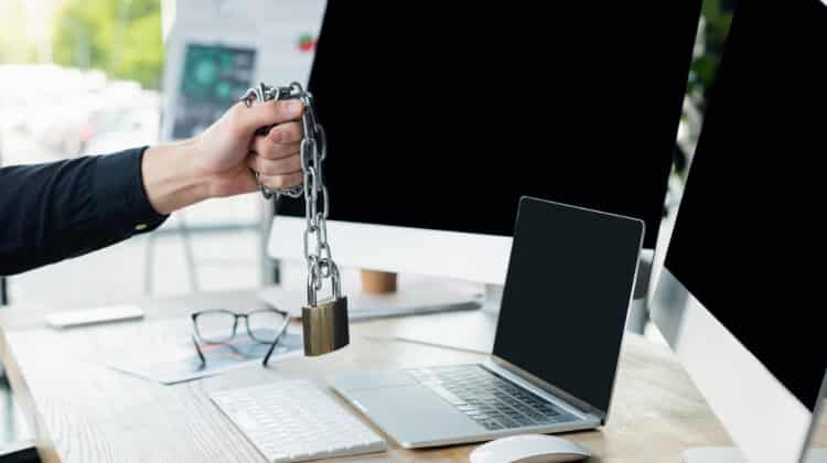 Cropped view of programmer holding padlock on chain near computers with blank screen in office