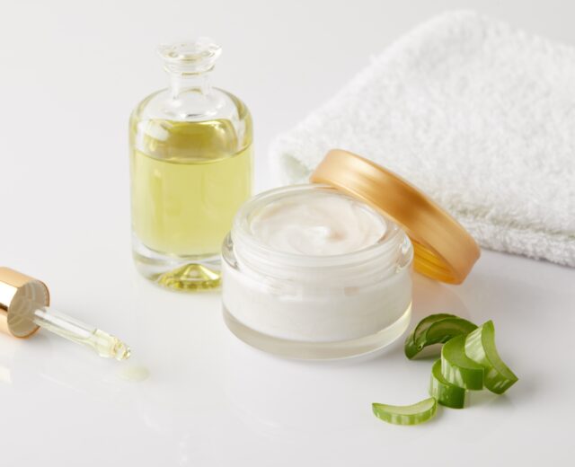 closeup shot of organic oil and cream, dropper, towel and aloe vera slices