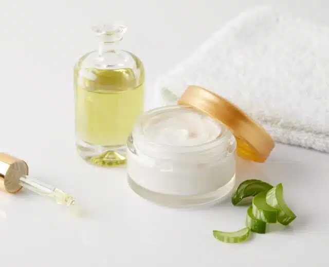 closeup shot of organic oil and cream, dropper, towel and aloe vera slices