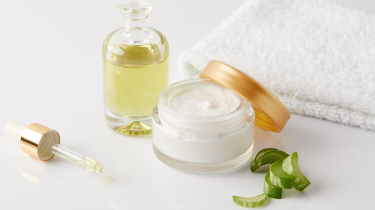 closeup shot of organic oil and cream, dropper, towel and aloe vera slices