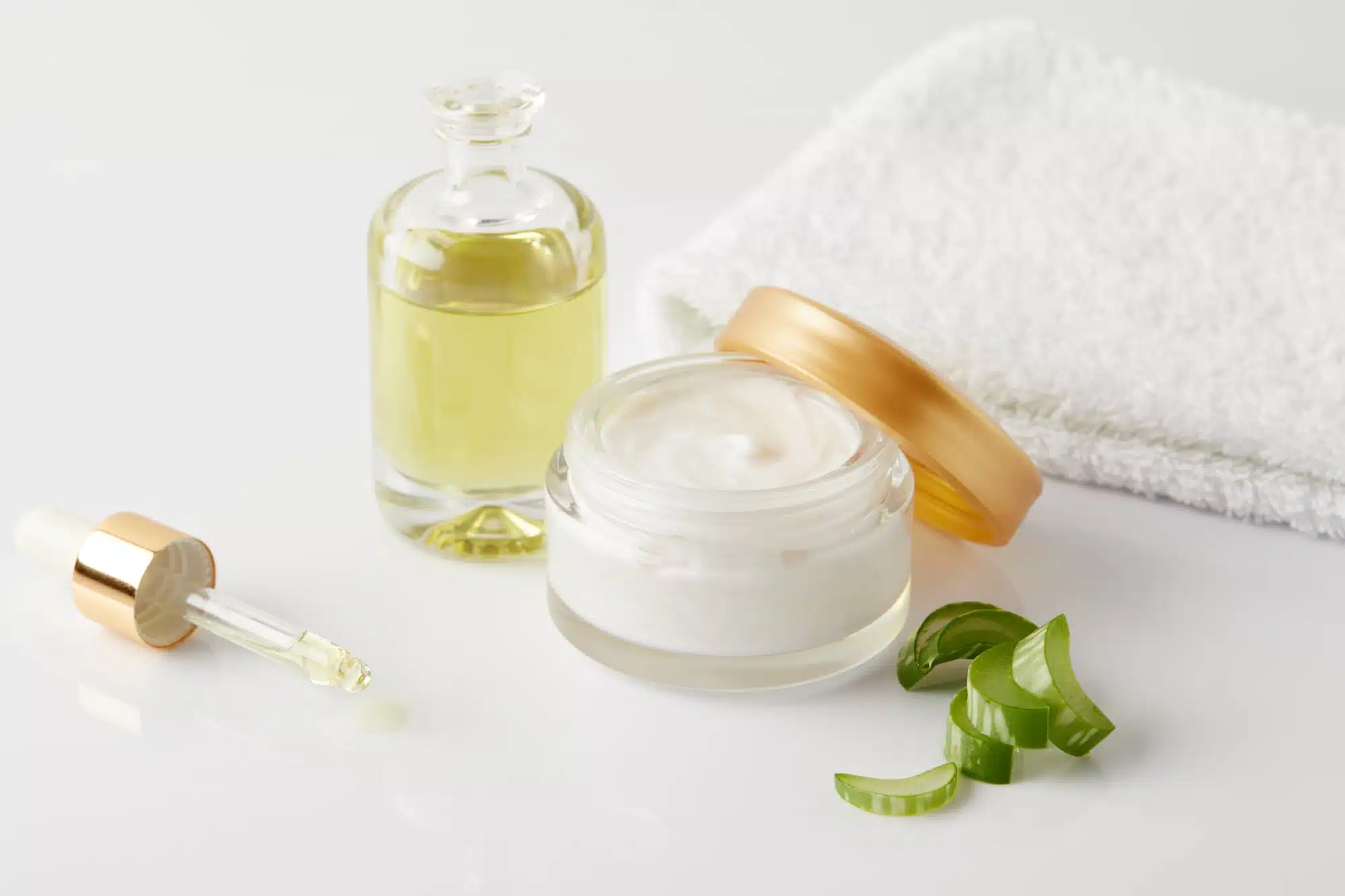 closeup shot of organic oil and cream, dropper, towel and aloe vera slices